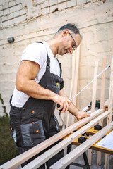 Mature male carpenter measuring wooden plank outdoors