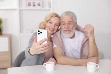 Obraz premium Senior man and mature woman taking selfie at home, selective focus. Happy couple