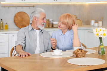 Lovely senior couple having breakfast together at wooden table in kitchen