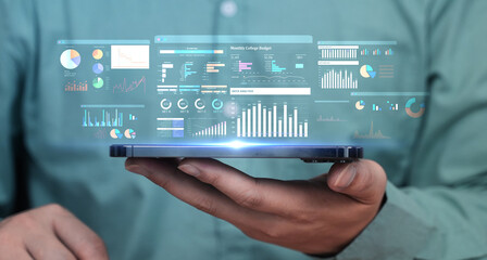 Business man holding tablet with a projected digital interface showing business analytics, charts,...