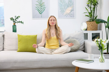 Feng shui. Young woman meditating on couch at home