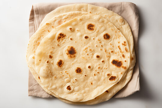 Stack of soft wheat chapatis on white cloth with rustic texture