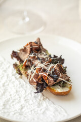 Bruschetta with roast beef and greens on white plate