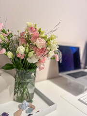 Fresh bouquet of pink and white flowers in a clear vase on a minimalist desk with a laptop and decorative stones, creating a serene workspace atmosphere