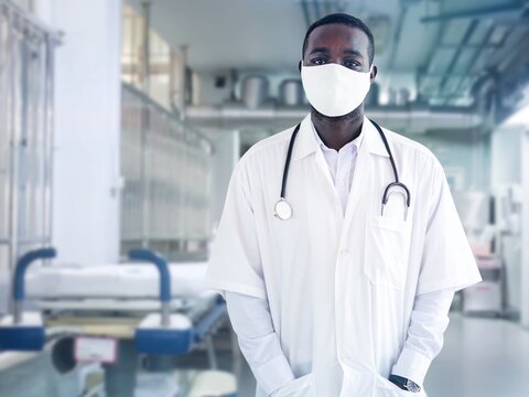 Portrait of an African male doctor wearing a face mask and standing in a lab coat with a portable stethoscope