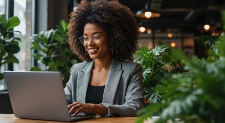 Smiling professional African American woman working on laptop in bright modern office with plants