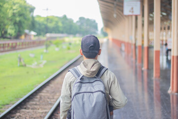 Young man standing alone at sunrise, standing on train station platform, holding map, confused but...