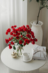 red roses in a vase stand on a white table next to a book and a cup of tea or coffee, in a white studio location or room for an advertising shoot or photo shoot