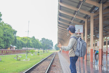 Young man standing alone at sunrise, standing on train station platform, holding map, confused but...