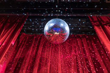 Disco ball reflecting light in a vibrant venue with red curtains