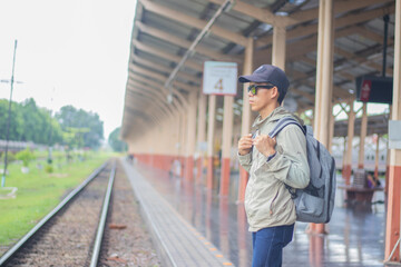 Young man standing alone at sunrise, standing on train station platform, holding map, confused but...