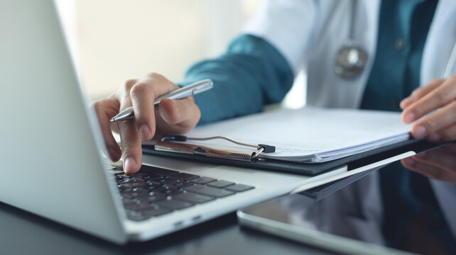 Doctor working on laptop computer and preparing patient's information for meeting with medical team. Doctor doing medical health record and medical prescription, insurance claim form