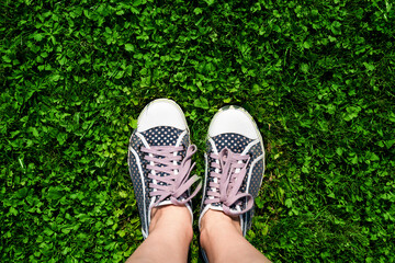 Woman's legs in sneakers on green grass. Concept of summer recreation in nature. Top view. Copy spase.