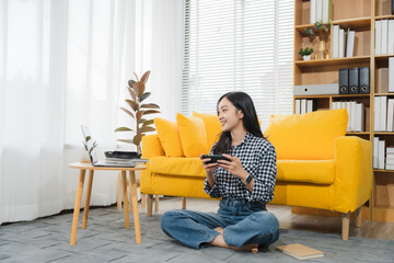Woman playing video games at home: A young woman smiles happily as she sits cross-legged on the...