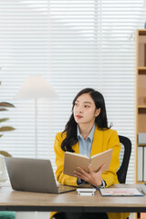 Businesswoman Planning Strategy: A focused young businesswoman in a yellow blazer sits at her desk,...