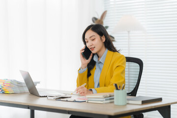 Focused Professional: A young woman in a vibrant yellow blazer engages in a phone call at her desk,...