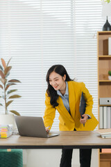 Young Businesswoman Working on Laptop: A cheerful young businesswoman in a yellow blazer leans over...