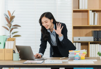 Smiling Greetings: A confident business woman extends a friendly wave during a virtual meeting, dressed in professional attire, showcasing modern office life and effective remote communication.