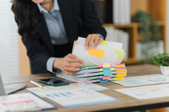 Businesswoman Managing Documents: A focused professional organizes and reviews important documents in a modern office environment, with attention to detail, this image reflects a dedicated workspace.