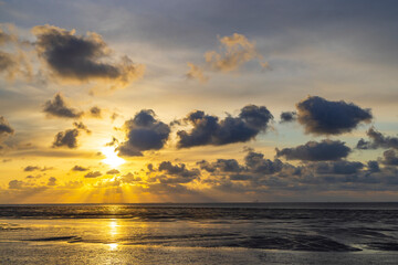 Golden sun setting over calm sea with scattered clouds creating beautiful light rays