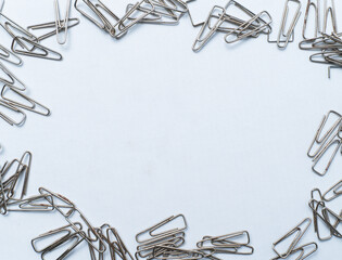 Flat lay of silver paper clips forming a border on a clean white background with copy space in the center. Ideal for office, stationery, or minimal background concepts.