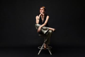 Beautiful woman in stylish outfit sitting on chair against black background