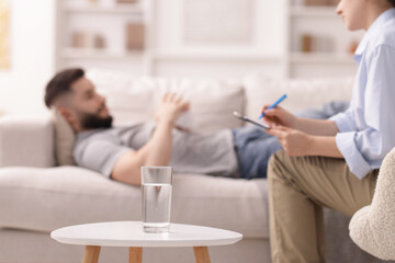 Professional psychologist working with patient in office, focus on glass of water