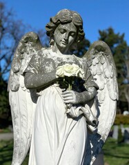 Weathered stone angel holding flowers, cemetery backdrop, sunny day