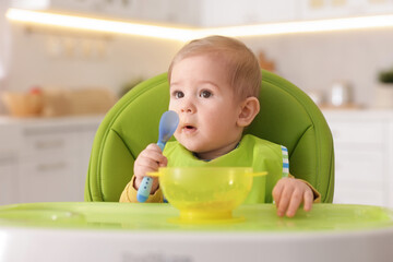Cute little baby eating healthy food in high chair indoors