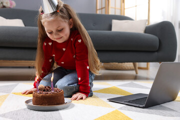 Birthday celebration. Little girl with cake having video call via laptop at home