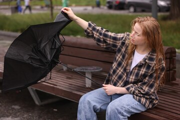 Woman with broken umbrella on bench outdoors
