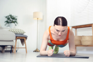 Young woman in sportswear doing plank exercise at home. Space for text
