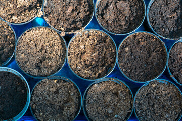 Plastic pots filled with dirt. The dirt is brown and the pots are blue. The dirt is in the shape of...