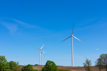 Modern wind turbines generating renewable energy on a clear day, surrounded by fields and trees,...