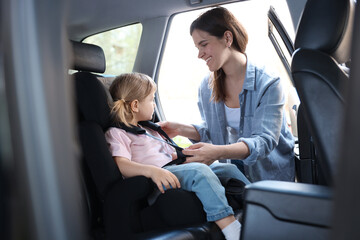 Happy mother fastening her daughter in child safety seat inside car