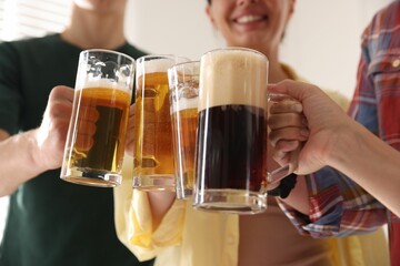 Friends clinking glass mugs of beer indoors, low angle view