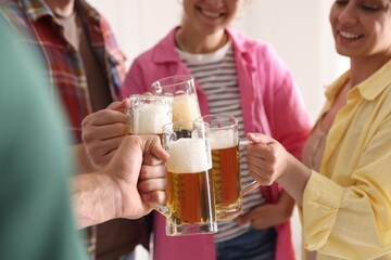 Friends clinking glass mugs of beer indoors, closeup