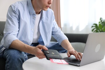 Man with passport and flight tickets using laptop at table indoors, closeup