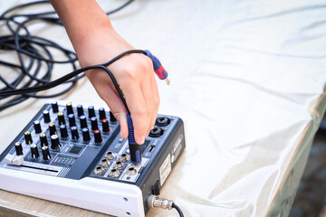 Hand connecting audio cable to sound mixer on wooden table. Concept of podcast setup, live event...