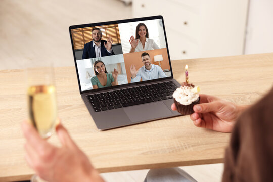 Celebrating birthday online. Man with sparkling wine and cupcake having video call with friends via laptop at home, closeup