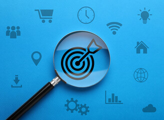 Magnifying glass over target with arrow on blue background, top view. Different icons around