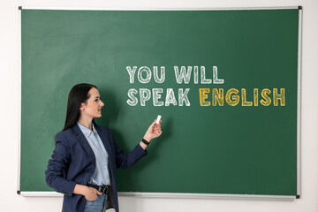 Teacher pointing at text You Will Speak English on green chalkboard. Language course