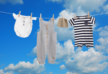 Different baby clothes drying on washing line against blue sky