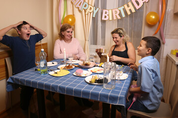 A woman with her son, sister, and nephew celebrates a birthday at a festive table. Soft lighting.