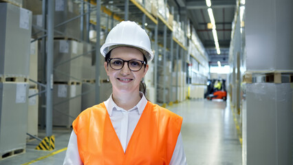 Headshot of a smiling industrial operator in a safety helmet and reflective vest, working in a busy cargo warehouse. She represents precision and reliability in global supply chains.