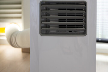 A portable white air conditioner on wheels, with an exhaust hose connected to the window