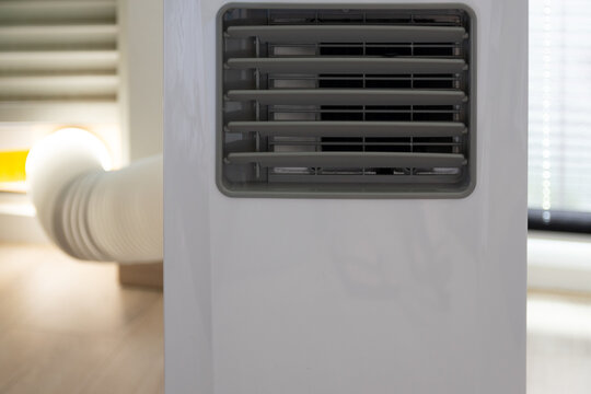 A portable white air conditioner on wheels, with an exhaust hose connected to the window