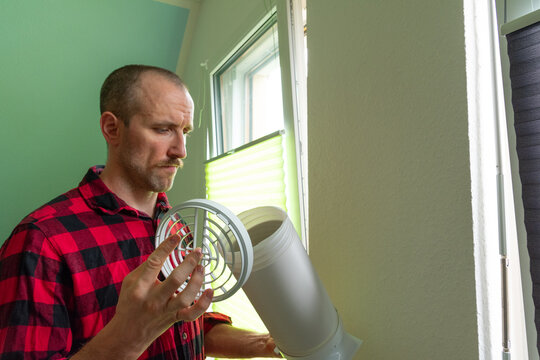A white man installing the hose of a portable air conditioner at home, close-up