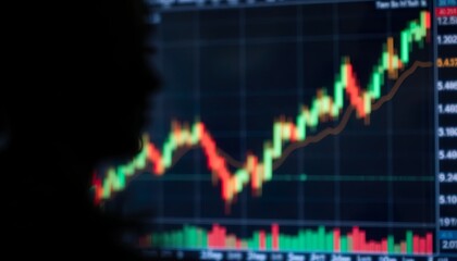 A Blurred Silhouette of a Person is Seen in The Foreground With a Background of a Stock Market Chart Displaying a Fluctuating Trend Line in Red and Green