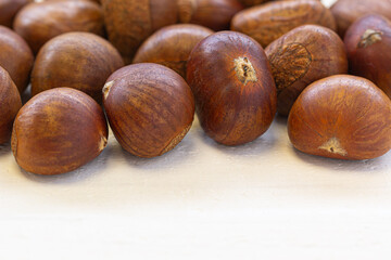 Natural brown chestnuts scattered on white rustic wood, ideal for food themes, autumn concepts, and healthy eating visuals.
